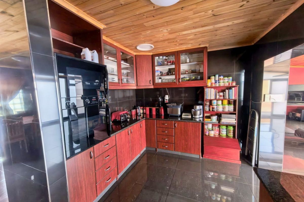 A functional kitchen featuring dark cabinetry, granite countertops, and a distinctive timber-clad ceiling with tiled flooring.