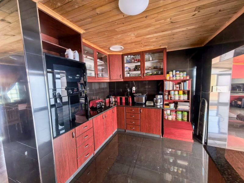 A functional kitchen featuring dark cabinetry, granite countertops, and a distinctive timber-clad ceiling with tiled flooring.