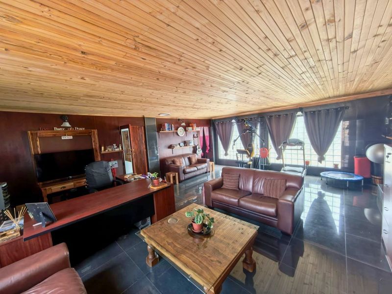 Spacious living area featuring a warm timber tongue and groove ceiling, dark tiled flooring, and large glass block windows providing natural light.