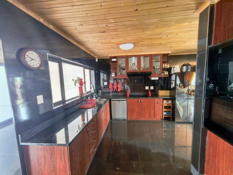 A well-appointed kitchen featuring dark cabinetry, granite countertops, a double sink, and a distinctive timber-clad ceiling with modern tiled flooring.