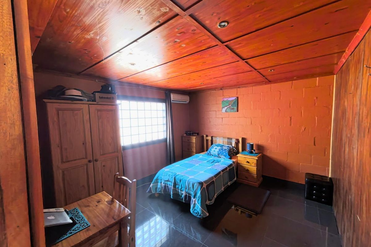 A bedroom featuring a timber-paneled ceiling, exposed brick walls, tiled flooring, and a glass block window with an integrated air conditioning unit.