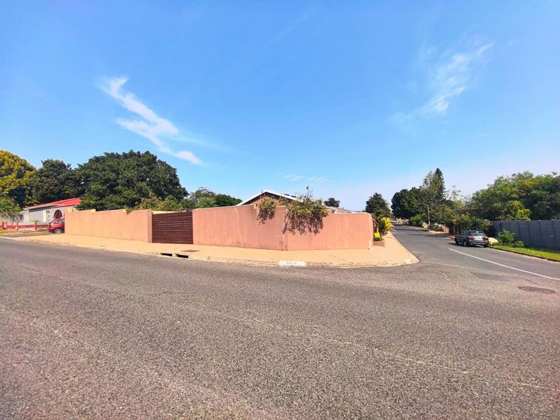 A street-level view of the property corner, featuring a solid perimeter wall and gated entrance from the road.