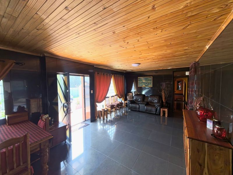 Spacious living area featuring a warm timber tongue and groove ceiling, dark wall paneling, and polished ceramic floor tiles with direct outdoor access.