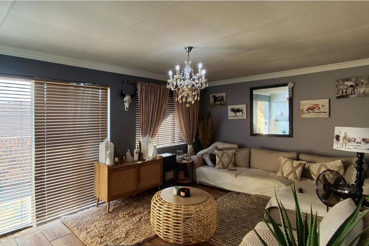 A cozy living room featuring a crystal chandelier, venetian blinds, and a sliding glass door providing natural light.