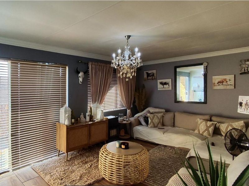 A cozy living room featuring a crystal chandelier, venetian blinds, and a sliding glass door providing natural light.