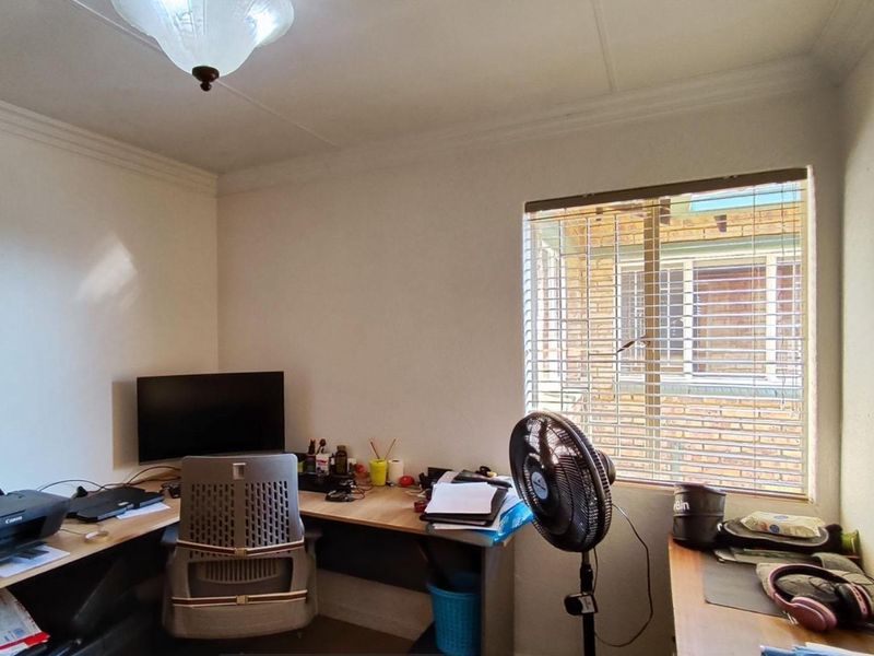 A functional home office space featuring neutral walls, coving, and venetian blinds on the window, providing a practical area for work or study.