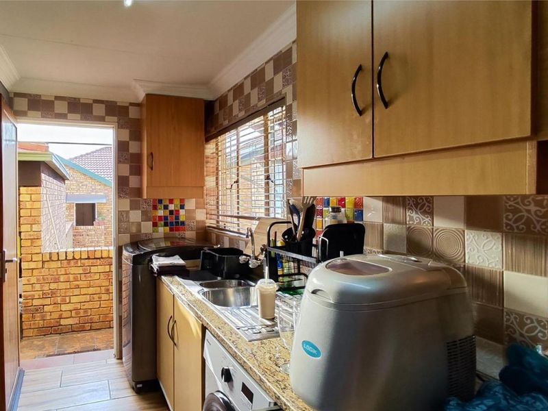 A functional scullery area featuring laminate cabinetry, granite countertops, a stainless steel sink, and decorative tiled backsplash with direct access to an outdoor patio.