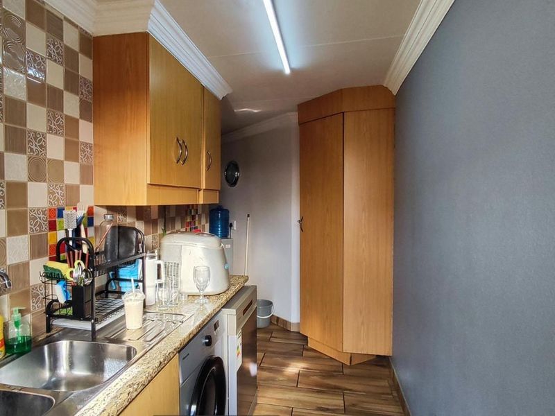 A functional scullery area featuring built-in wooden cabinetry, a stainless steel sink, tiled backsplash, and durable laminate flooring.