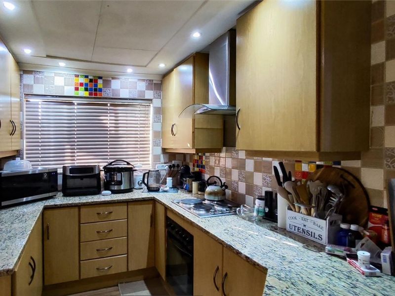 A functional kitchen featuring granite countertops, built-in wooden cabinetry, an electric hob with extractor fan, and a tiled backsplash.