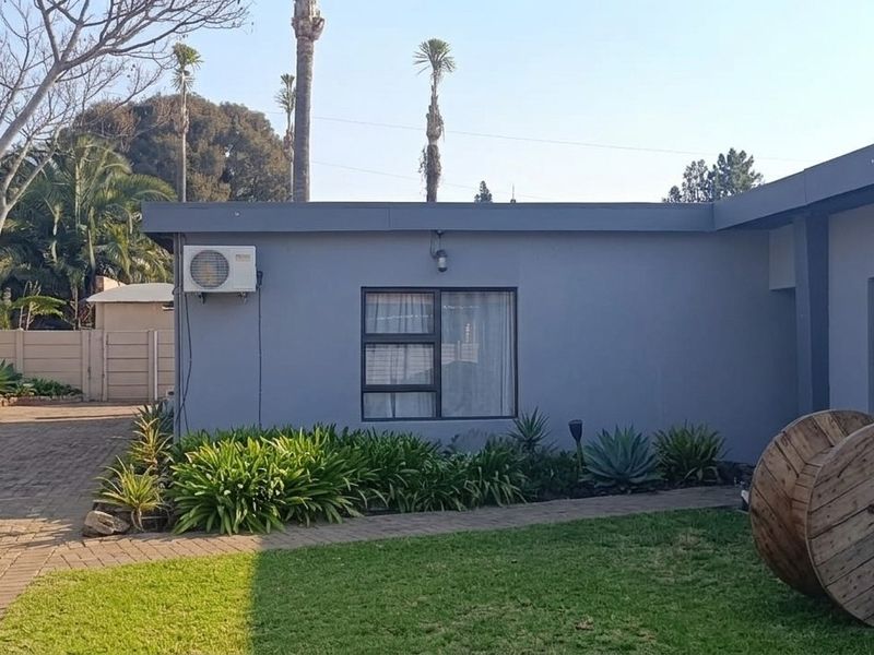Rear exterior view of the property featuring a paved driveway, landscaped garden beds, and modern grey painted exterior walls with aluminium window frames.
