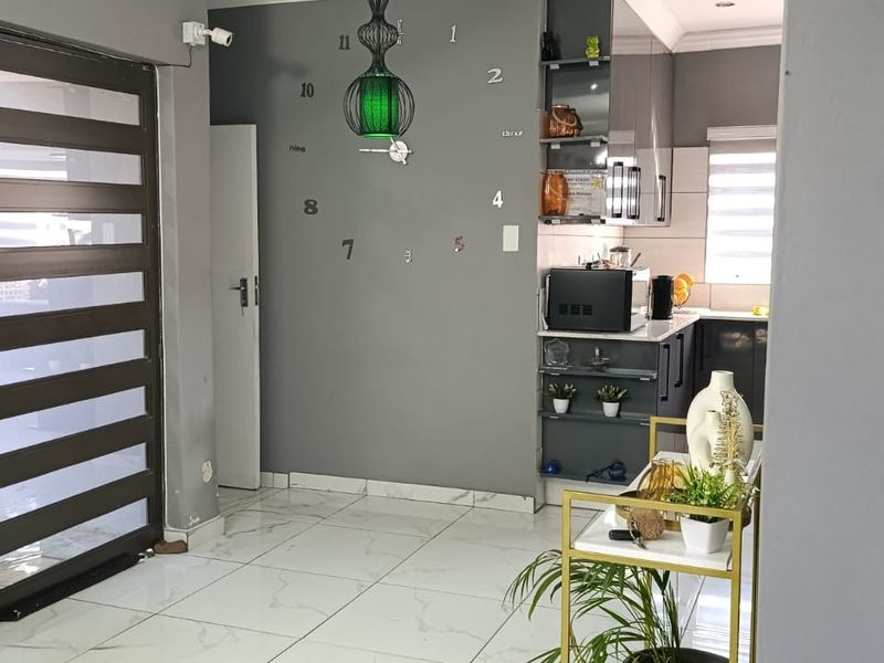Open plan living area featuring modern tiled flooring, a secure entrance door, and a compact kitchen space with built-in cabinetry.