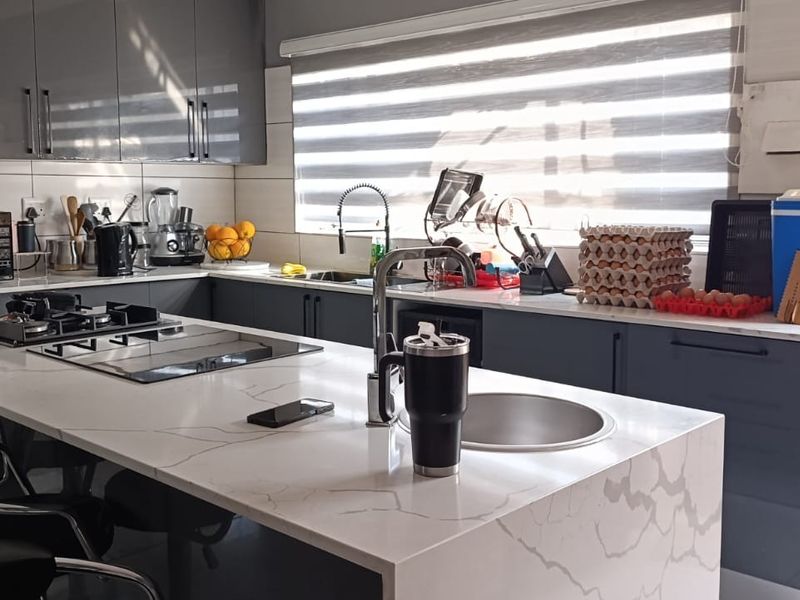 Modern kitchen featuring a central island with quartz countertops, high-gloss cabinetry, built-in hob, and a sleek undermount sink with a gooseneck faucet.