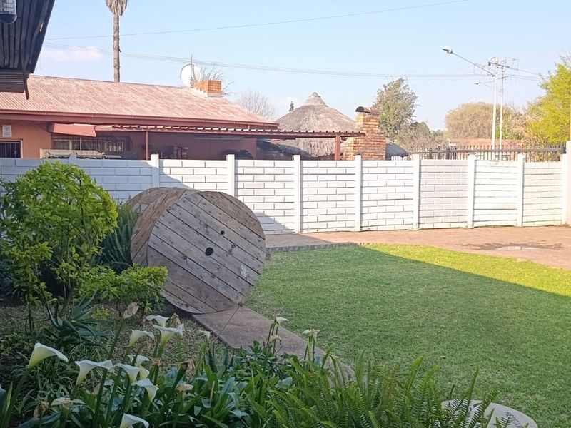 A view of the rear garden area featuring a paved driveway, a secure sliding gate, and a precast concrete boundary wall.