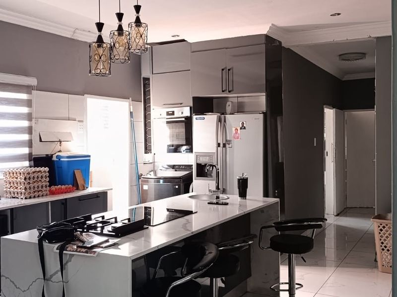 Modern kitchen featuring a central island with a built-in hob, sleek cabinetry, integrated appliances, and tiled flooring with contemporary pendant lighting.