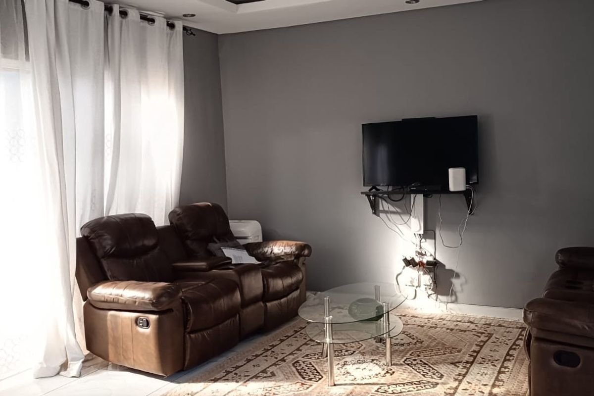 A living room featuring grey walls, recessed ceiling lighting, and a sliding glass door with curtains.
