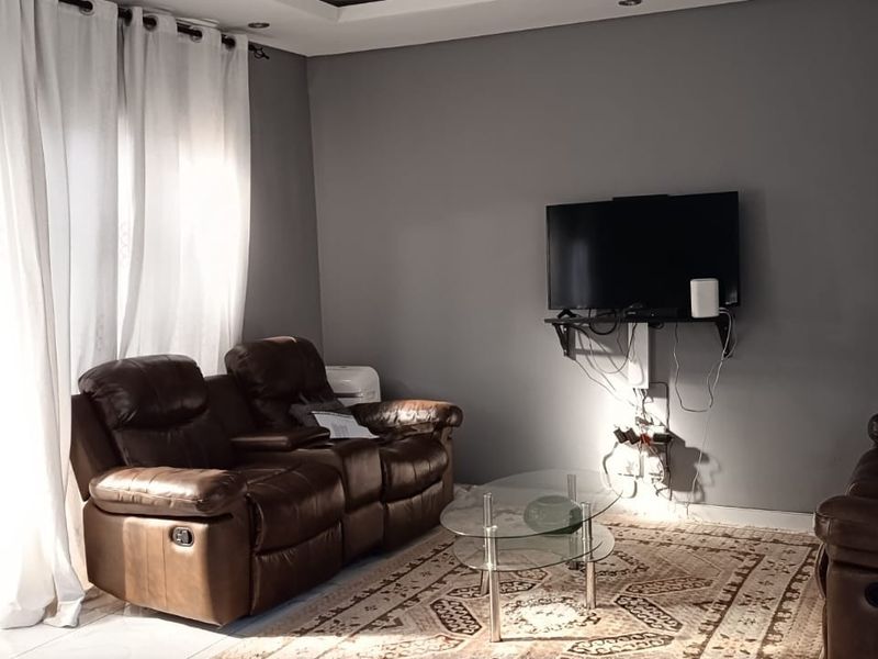 A living room featuring grey walls, recessed ceiling lighting, and a sliding glass door with curtains.