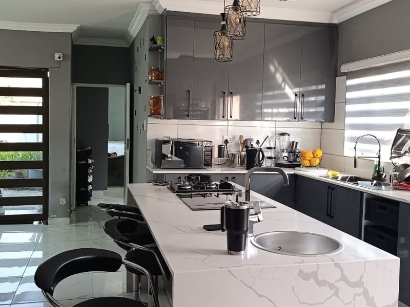 Modern kitchen featuring a large central island with quartz countertops, high-gloss cabinetry, built-in gas hob, and sleek porcelain floor tiles.