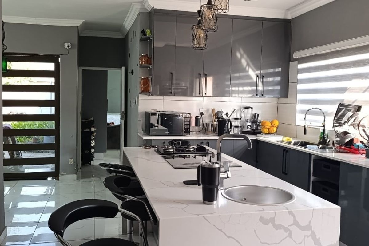Modern kitchen featuring a large central island with quartz countertops, high-gloss cabinetry, built-in gas hob, and sleek porcelain floor tiles.