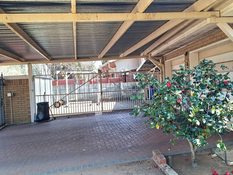 A covered carport area featuring brick paving, a corrugated metal roof, and secure metal gate access.