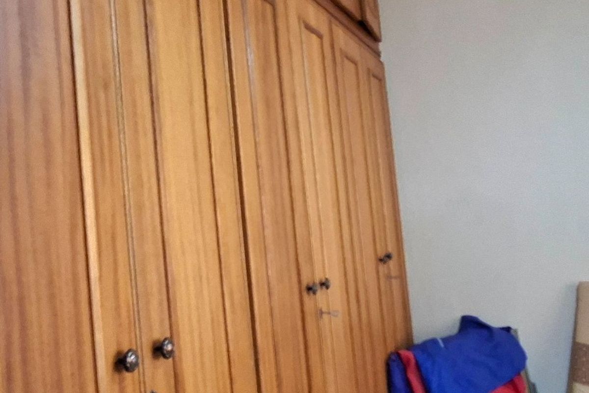 A bedroom featuring floor-to-ceiling built-in wooden cupboards with integrated overhead storage compartments.