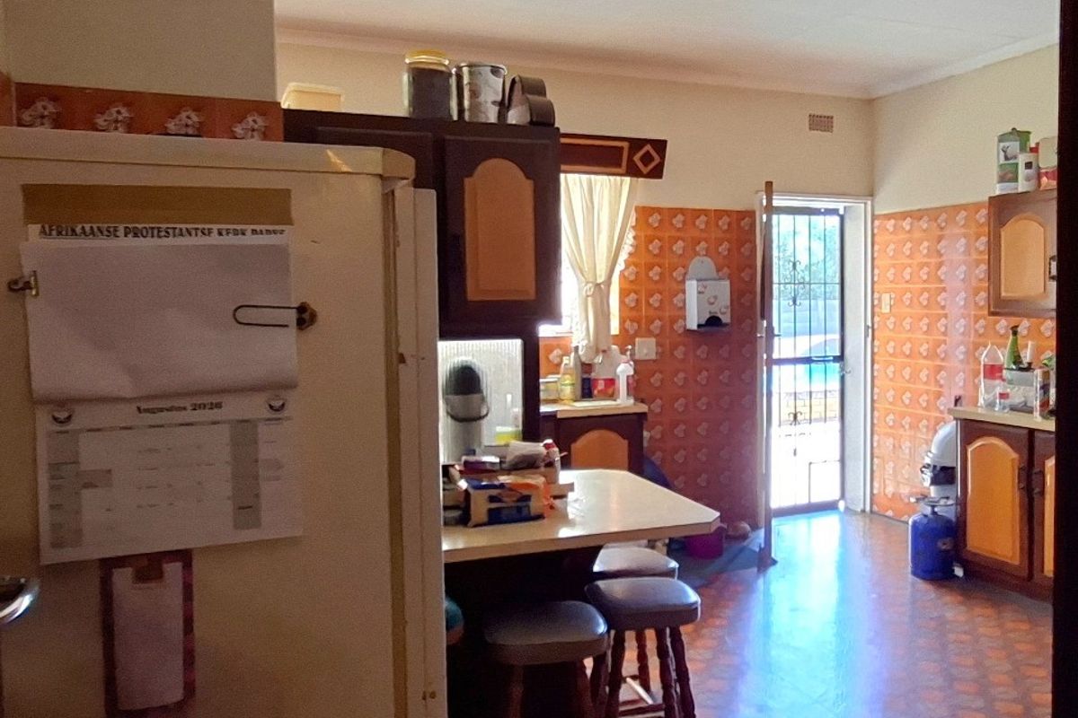 A dated kitchen featuring traditional cabinetry, patterned wall tiles, and tiled flooring, with direct access to the exterior through a security gate.