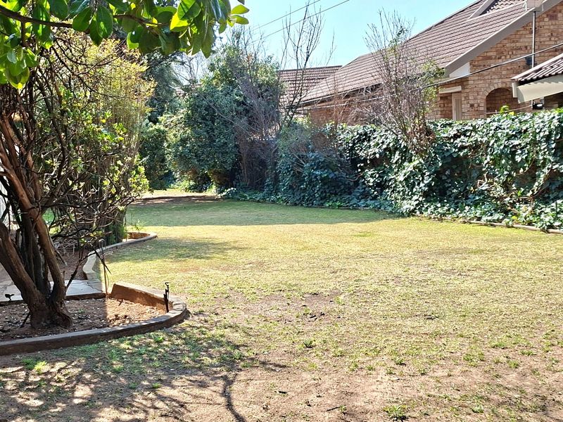 A spacious rear garden featuring a large lawn area, mature trees, and a brick-edged garden bed with an ivy-covered boundary wall.
