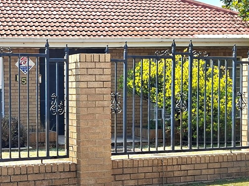 Front view of a brick house featuring a tiled roof and secure wrought iron fencing with a brick boundary wall.