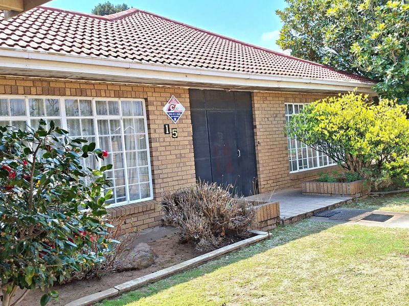 Front facade of a face brick house featuring a tiled roof, security gate, and established garden beds with paved walkway access.