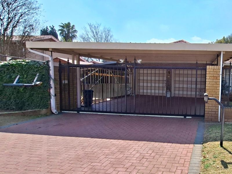 Front exterior view featuring a paved driveway, a covered carport, and a secure wrought iron gate entrance.