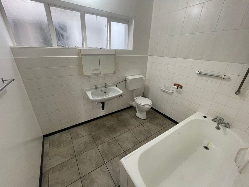 A functional bathroom featuring a bathtub, wall-mounted basin, and toilet with tiled finishes, offering a blank canvas for potential modernization and renovation.