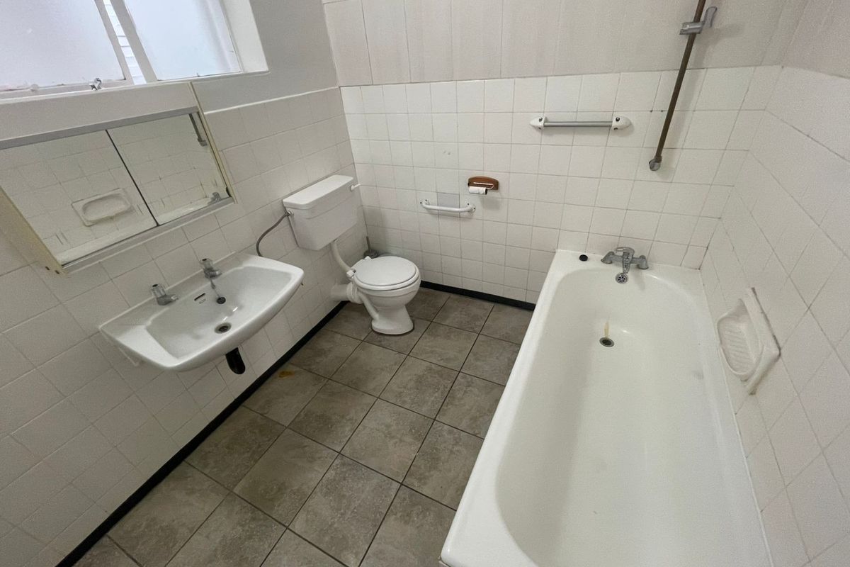 A functional, dated bathroom featuring a bathtub, wall-mounted basin, and toilet with tiled finishes, offering potential for modernization and renovation.