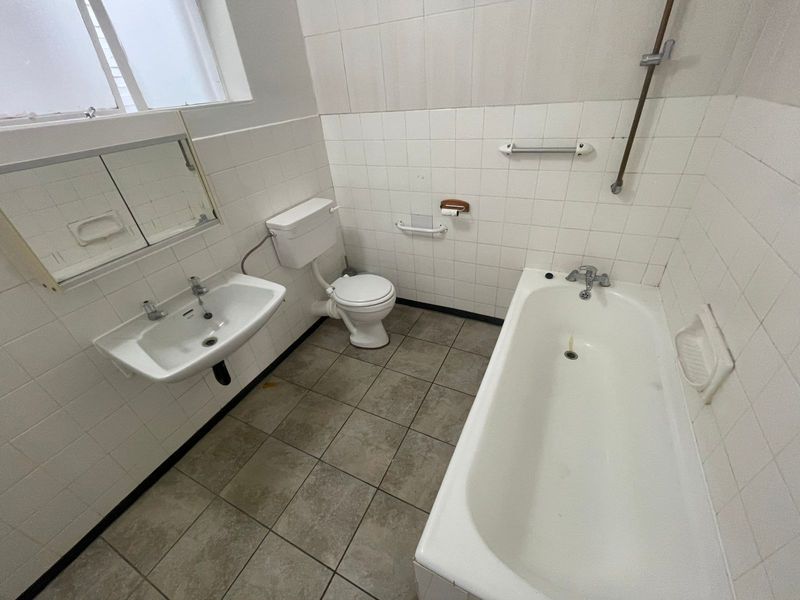 A functional, dated bathroom featuring a bathtub, wall-mounted basin, and toilet with tiled finishes, offering potential for modernization and renovation.
