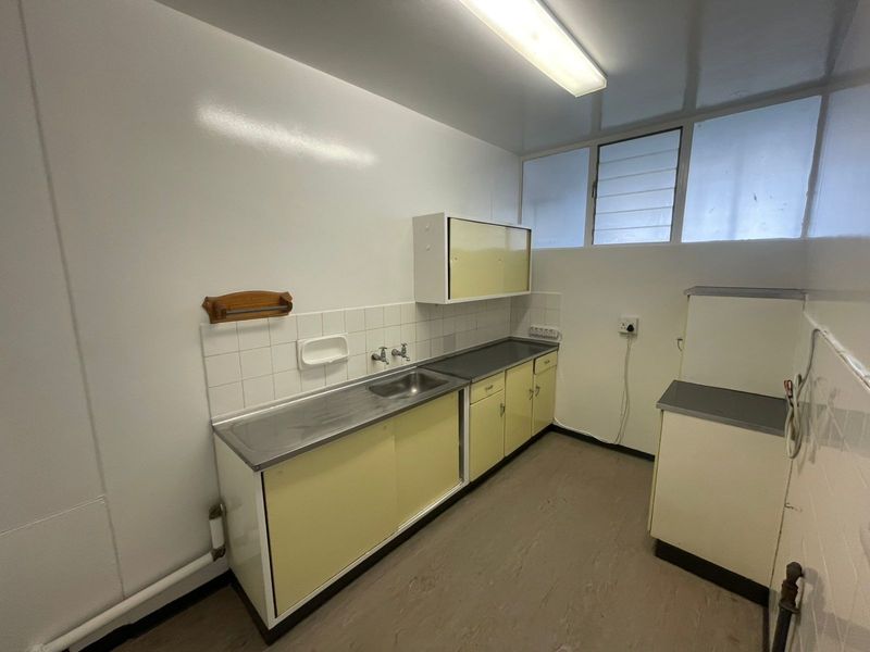 A functional laundry room featuring built-in cabinetry, a stainless steel sink, tiled splashback, and louver windows, offering a clean and practical utility space.