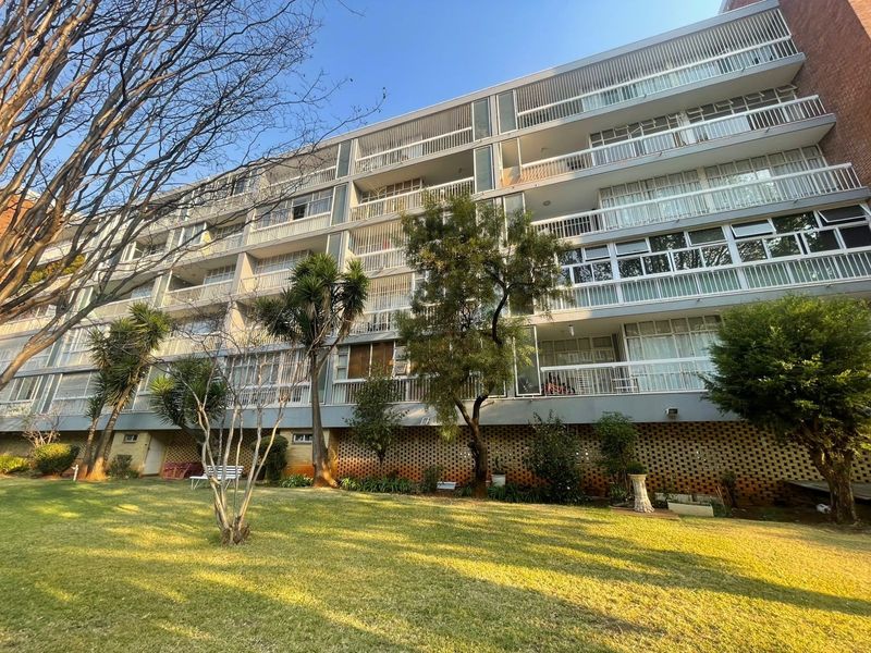 A view of the rear apartment building facade featuring multiple levels of balconies with metal railings and a well-maintained communal garden area.