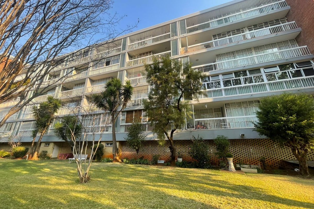 A view of the rear apartment building facade featuring multiple levels of balconies with metal railings and a well-maintained communal garden area.