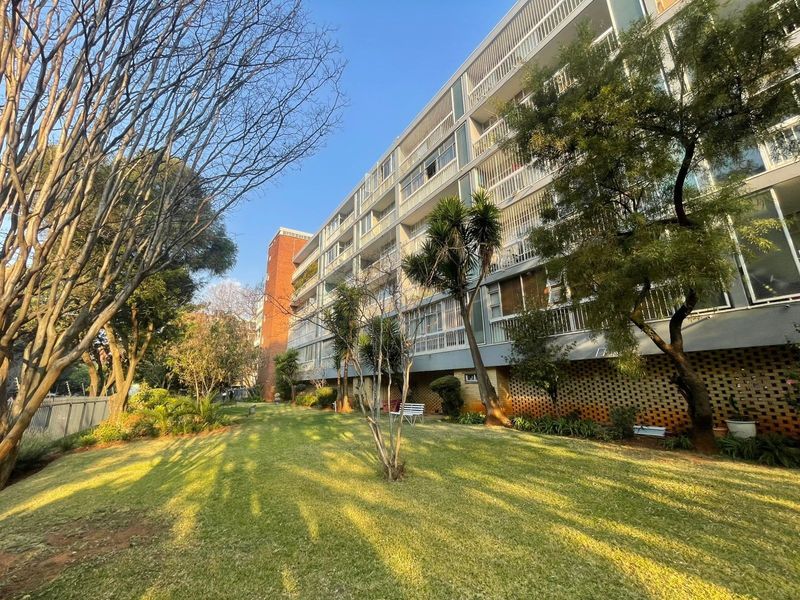 A view of the apartment building's rear facade featuring multiple levels of balconies overlooking a well-maintained communal garden area.