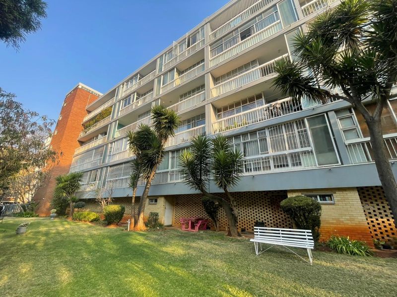 Rear view of a multi-story apartment building featuring private balconies, brick facade detailing, and access to a shared garden area.
