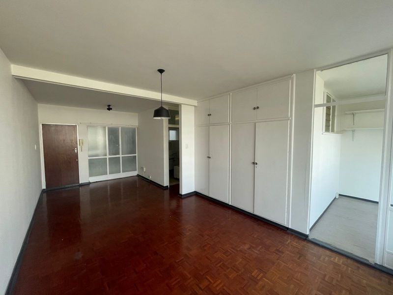 Spacious living area featuring original parquet flooring, extensive built-in storage cupboards, and a neutral interior layout ready for personalization.