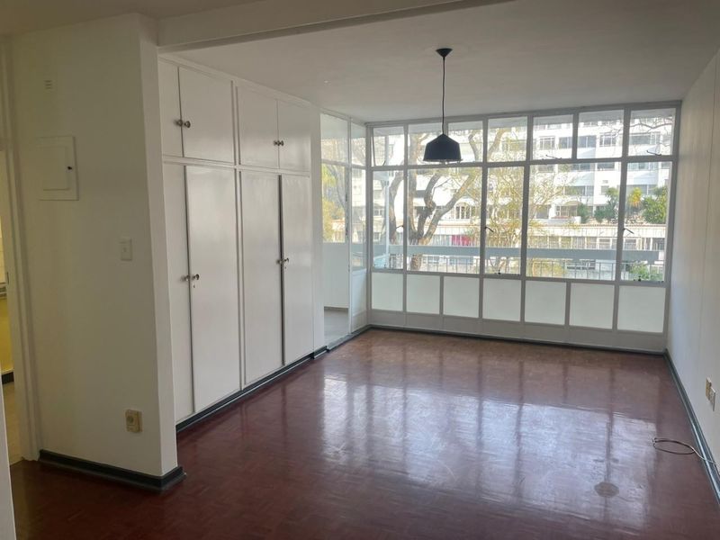 Bright and spacious living area featuring original parquet flooring, extensive built-in storage cupboards, and large windows providing ample natural light.