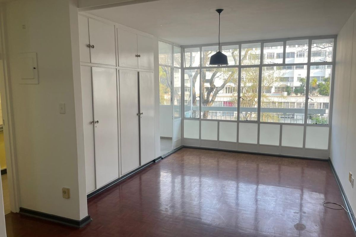 Bright and spacious living area featuring original parquet flooring, extensive built-in storage cupboards, and large windows providing ample natural light.