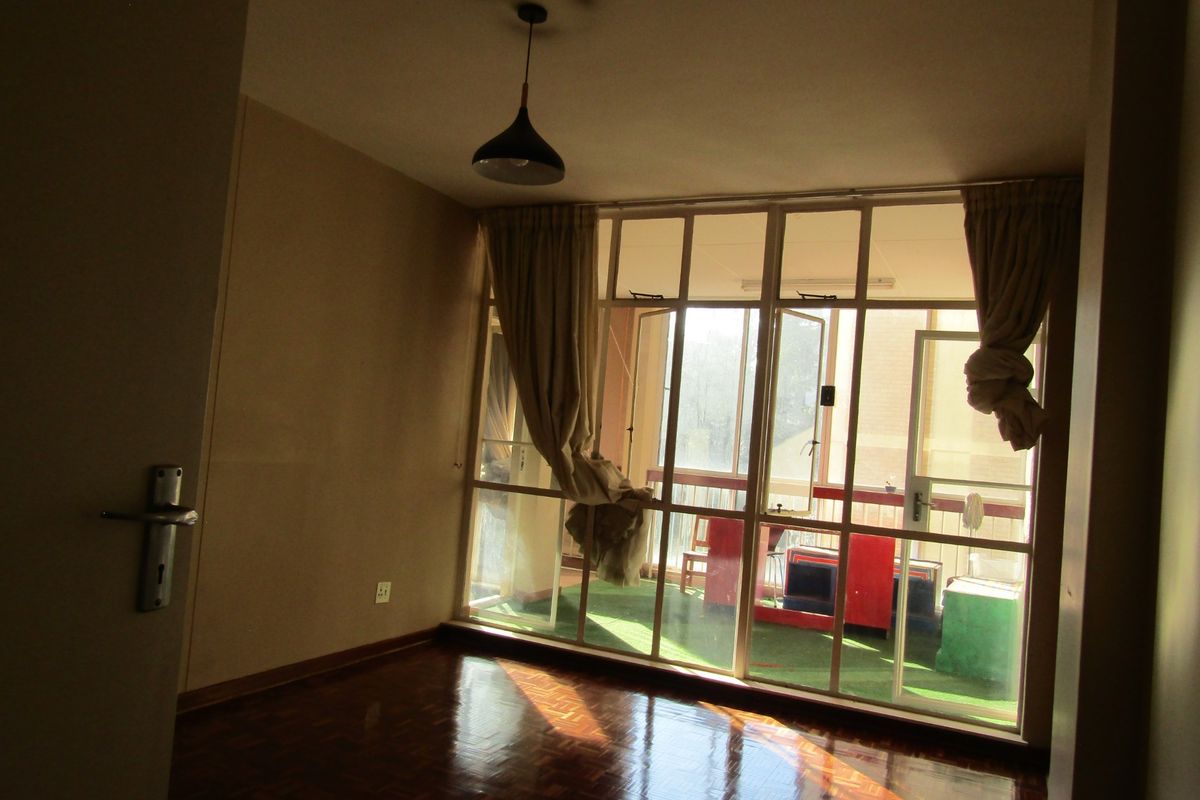 An empty living room featuring polished parquet flooring, a pendant light fixture, and large glass doors providing access to an attached balcony.