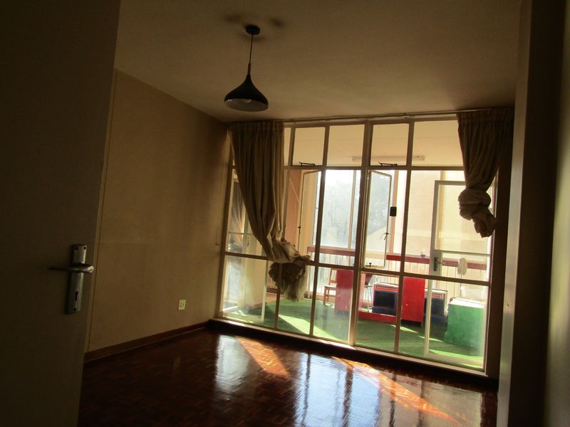 An empty living room featuring polished parquet flooring, a pendant light fixture, and large glass doors providing access to an attached balcony.