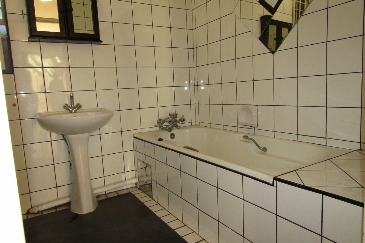 A dated bathroom featuring a pedestal basin, built-in bathtub, and white tiled walls. The space requires modernization of fixtures and finishes.