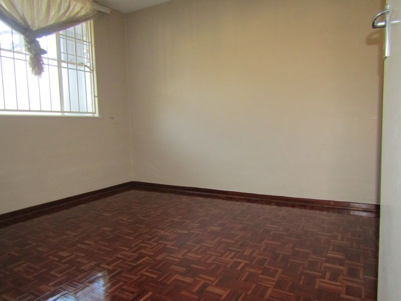 An empty bedroom featuring polished parquet flooring, neutral walls, and a window fitted with security bars.