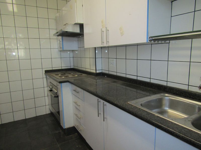 A functional kitchen featuring built-in white cabinetry, dark granite countertops, a stainless steel sink, and integrated cooking appliances with tiled wall finishes.