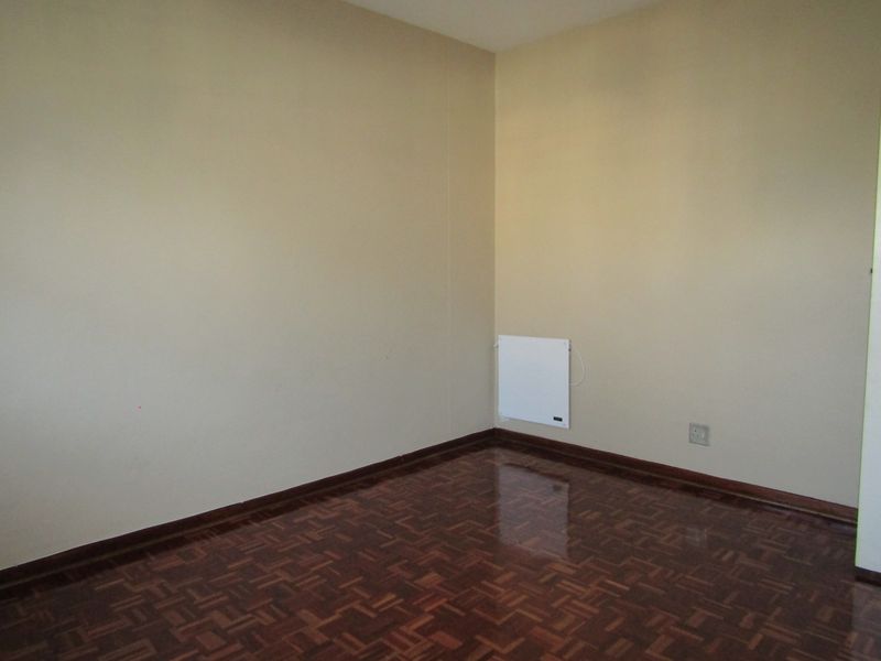 An empty bedroom featuring polished parquet flooring, neutral wall finishes, and a wall-mounted electric heater.