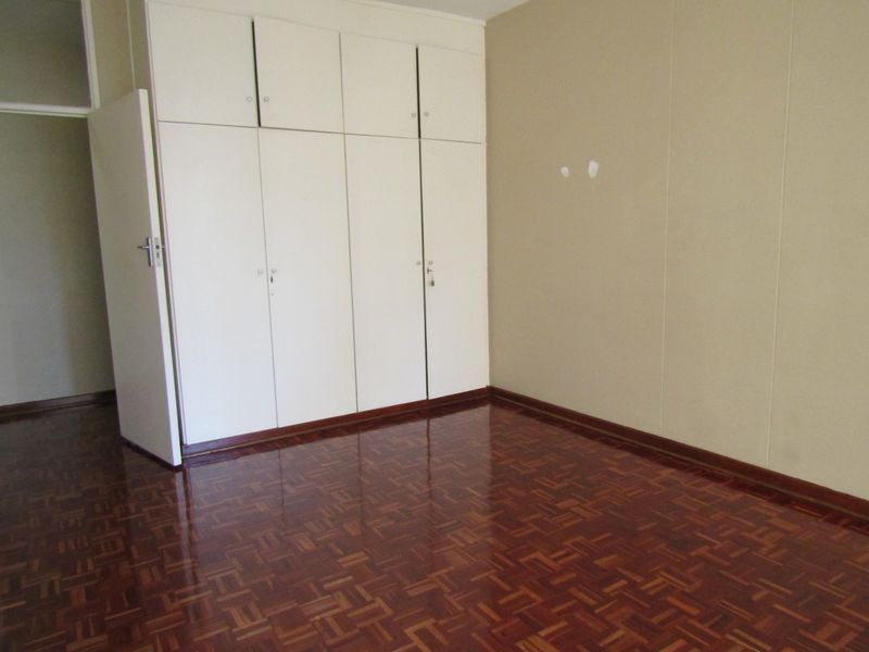 A vacant bedroom featuring polished parquet flooring and floor-to-ceiling built-in cupboards, offering a clean canvas for personalization.