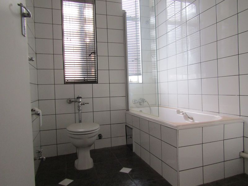 A functional bathroom featuring white wall tiles, a bathtub with a glass screen, and a flush toilet.