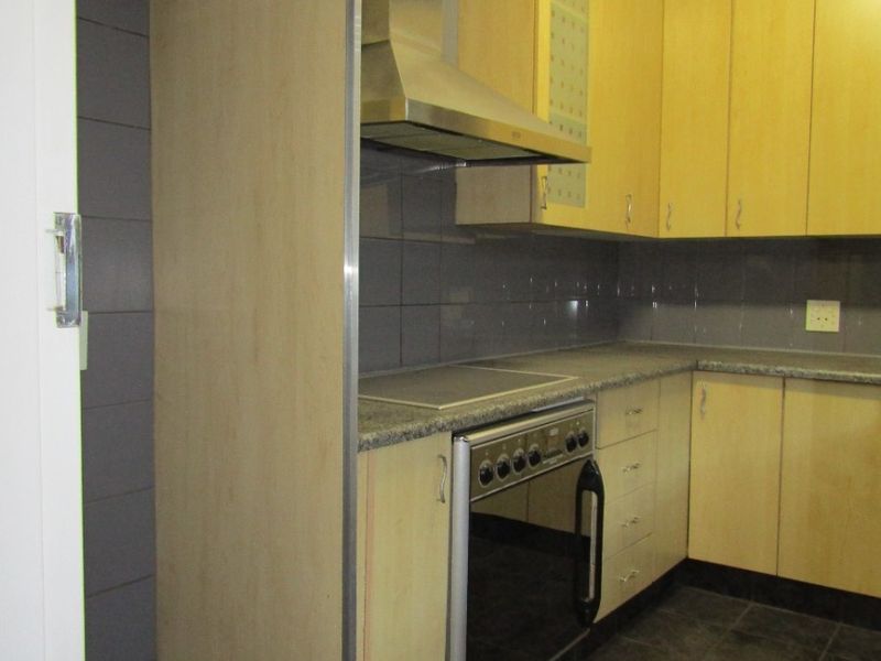 A functional kitchen featuring light wood cabinetry, stone countertops, a built-in stove with extractor fan, and dark tiled flooring.