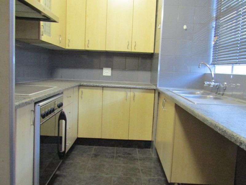 A functional kitchen featuring light wood-tone cabinetry, granite-look laminate countertops, a built-in oven with hob, and dark tiled flooring.